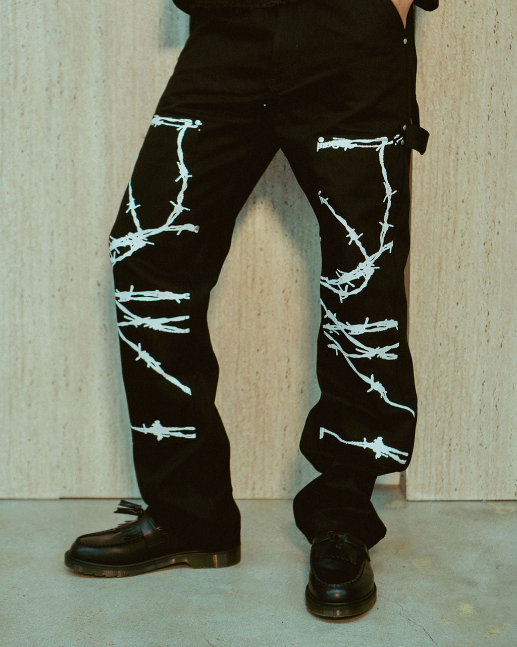 Barbed Wire Carpenter Jeans - black carpenter pants with white barbed wire graphic printed along the legs and double knee area, featuring carpenter loop detailing