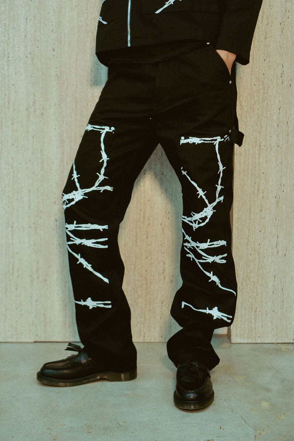 Barbed Wire Carpenter Jeans - black carpenter pants with white barbed wire graphic printed along the legs and double knee area, featuring carpenter loop detailing